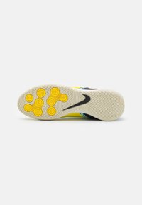 Żółta podeszwa sportowego buta z czarnymi akcentami. Posiada okrągłe wzory chwytne oraz teksturowaną białą wkładkę dla lepszej przyczepności i stabilności.