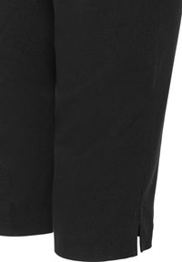 Gros plan sur un pantalon en tissu noir montrant la zone inférieure de la jambe avec une petite fente latérale près de l'ourlet.