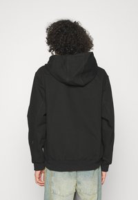 Schwarzer Hoodie aus weichem Stoff, mit Kapuze und Kordelzug, gerippten Bündchen und Saum sowie lockerem Schnitt. Keine sichtbaren Logos oder Muster.