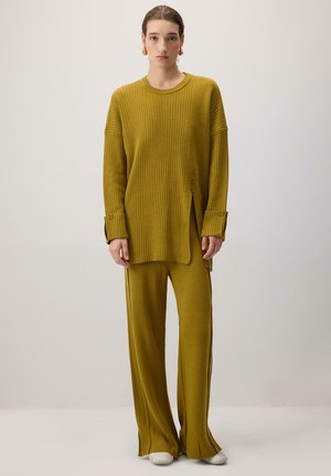 Senf žbiričasti džemper s bočnim gumbima, uparen s širokim hlačama koje se podudaraju. Oboje imaju teksturirani finiš i opušteni kroj.