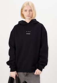 Black hooded sweatshirt made of cotton fleece. Features a central white logo with "CPH STUDIOS" text, oversized fit, and ribbed cuffs.
