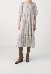 Long, flowing dress with short, sheer flutter sleeves. Light floral print in pastel colors on soft fabric. Paired with brown, heeled boots.