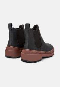 Stivali Chelsea in pelle nera con pannelli elastici laterali, suole in gomma marrone e dettagli testurizzati. Presentano un tirante sul retro per un facile utilizzo.