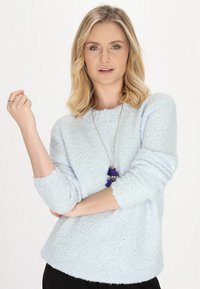 Pulover texturat, de culoare albastru deschis, cu decolteu rotund și mâneci trei sferturi, asociat cu un colier în mai multe straturi, care are franjuri albastre.