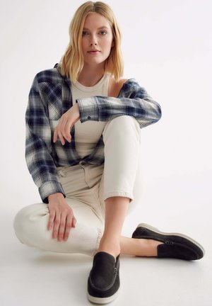 Plaid flannel shirt in navy and white, fitted tank top, light-colored jeans, and black slip-on shoes. Textured fabric and casual fit.