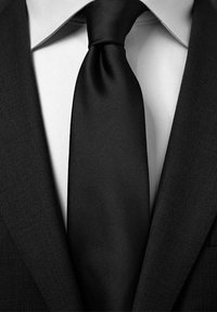 Svart satin slips knuten tätt vid kragen, ihop med en vit skjorta och en strukturerad svart kostymjacka. Ren, formell design.