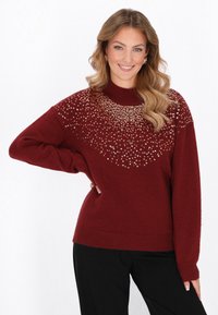 Maglione bordeaux con collo alto e complesse decorazioni di paillettes dorate sul petto, dotato di maniche lunghe e una vestibilità rilassata.