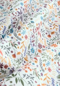 Bomuldsstof med en hvid baggrund, der har et heldækkende blomstermønster i forskellige farver, herunder orange, blå, lilla og grøn.