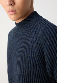 Maglione a coste blu navy con un colletto alto e dettagli testurizzati. Design aderente che enfatizza il motivo lavorato a maglia e la profondità del materiale.