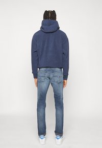 Námořnický modrý zkrácený mikina s velkou kapucí, spárovaná se světlými modrými slim-fit džíny. Významné detaily: zadní kapsy na džínách a bílé tenisky.