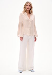 Lichtroze gestreepte blouse met belmouwen, knoopsluiting aan de voorkant, gecombineerd met witte wijde broek en blauwe platte schoenen. Gladde stoftextuur.