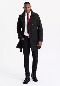 Czarny trencz z podwójnym zapięciem, dużymi guzikami, epoletami, w połączeniu z białą koszulą, czerwoną muchą i czarnymi dżinsami. Czarne sznurowane botki.