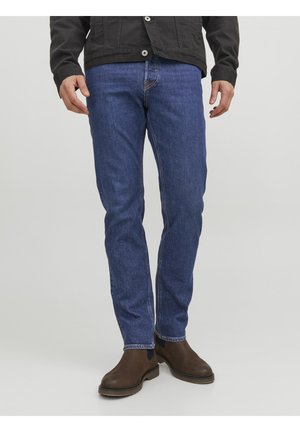 Dunkelblaue Jeans aus Denim mit geradem Schnitt, versehen mit heller Naht, Fronttaschen und abgetragenen braunen Lederstiefeln.