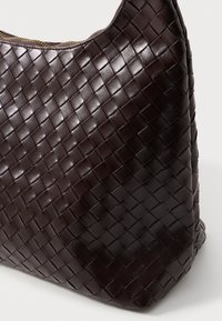 Mörkbrun läderväska med en vävd textur, som har en böjd topp och dragkedjestängning. Botten är platt och något strukturerad.