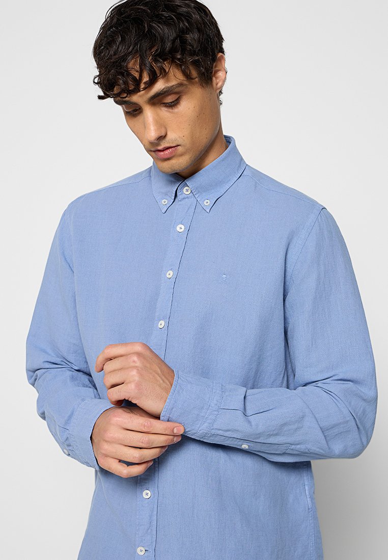 Camisa de manga larga azul clara hecha de una tela suave, con un cuello abotonado, botones en el frente y un pequeño logotipo en el pecho.