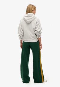 Grå hættebluse med løs pasform, parret med grønne vide bukser med gule sidelister. Enkle hvide sneakers fuldender looket.