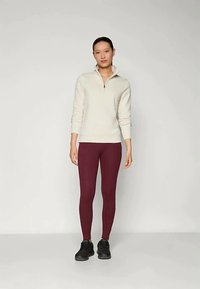 Felpa leggera grigia con zip, maniche lunghe, abbinata a leggings bordeaux e scarpe da ginnastica nere. Texture liscia, design aderente.