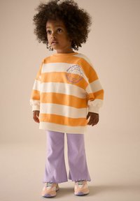 Pasiasty sweatshirt w kolorze pomarańczowym i kremowym, z grafiką, w połączeniu z fioletowymi spodniami z rozszerzanymi nogawkami i wielokolorowymi sneakersoni.