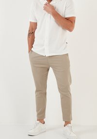 Biała koszula z krótkim rękawem, zapinana na guziki, o fakturowanej tkaninie, w połączeniu z jasnobeżowymi chinosami i białymi sneakersami, w fasonie slim-fit.