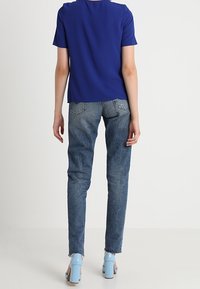 Modrá krátká halenka s krátkým rukávem spojená s vysokými, vybledlými modrými džíny. Dokončení zahrnuje třásně na spodním lemu a světle modré boty na blokovém podpatku.