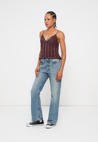 Bordo brezrokavni top z zvitim dizajnom in srebrnimi navpičnimi črtami, v kombinaciji z svetlo modrimi širokimi kavbojkami in črnimi supergami.