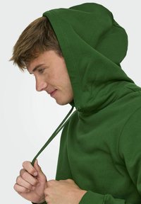 Felpa verde con cappuccio e cordino. Presenta una texture morbida e polsini a coste. Il design è semplice e adatto per un look casual.