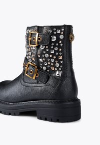 Czarne skórzane botki za kostkę z dwoma złotymi klamrami, ozdobione ćwiekami w srebrnych i różowych odcieniach oraz teksturowaną powierzchnią.