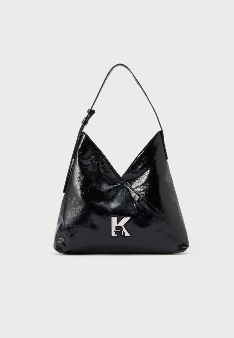 Melna lakādas plecu soma ar vienu siksnu un sudraba "K" logotipu priekšpusē uz vienkārša gaisīga fona.