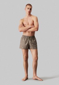 Bruine zwemshorts met een patroon in een rasterdesign en logo-accenten, voorzien van een elastische Tailleband en trekkoord.