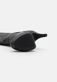 Černé kotníkové boty na vysokém podpatku s hladkým koženým povrchem, špičatou špičkou, žebrovanou podrážkou a elegantním designem. Ozdobeno štíhlým podpatkem.