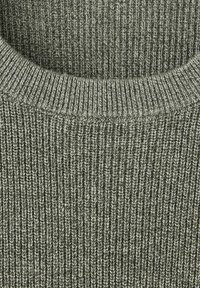 Gros plan d’un tissu tricoté côtelé doux gris avec un col arrondi, montrant la texture détaillée et le motif de couture.