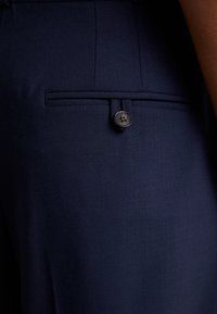 Námornícke nohavice s úzkym strihom, vyrobené z textúrovanej látky. Obsahujú zadnú vrecko so zatváraním na tmavé gombíky. Minimalistický dizajn.