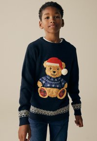 Maritimer Strickpullover mit einem strukturierten Teddybär in rotem Hut, blauer Jacke und karierten Akzenten, abgerundet mit einem gemusterten Saum.