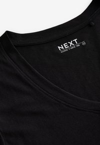 Schwarzes locker sitzendes V-Ausschnitt-T-Shirt, das den Halsausschnitt und das Innenschild mit dem Markennamen „NEXT“ und der Größe XS zeigt.