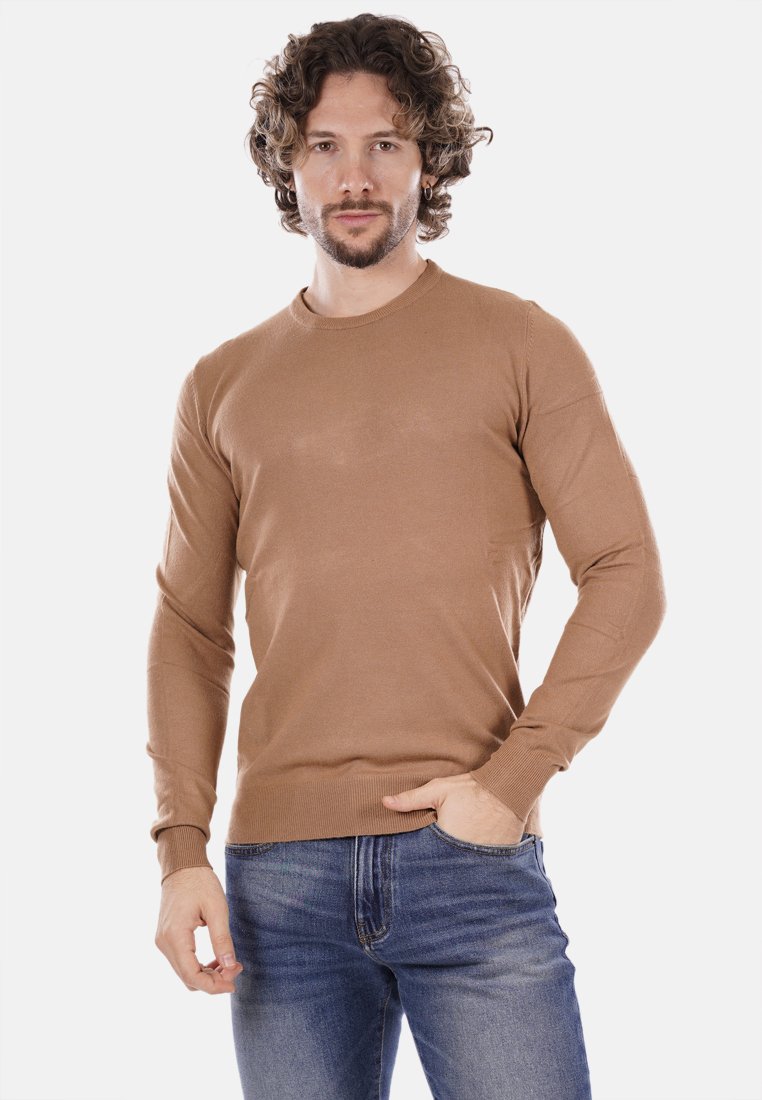Maglione lungo marrone chiaro, con maniche lunghe e collo rotondo, polsini a coste e una texture liscia. Indossato con jeans blu.