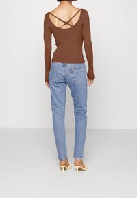 Brun ribbad långärmad topp med korsad rygg, kombinerad med ljusblå tapered jeans. Modellen bär ljusgula öppna klackar.