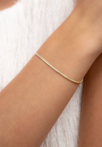 Bracelet jonc fin ton or avec une surface lisse et plate reposant sur une peau claire, mettant en valeur un design minimaliste.