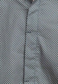 Camicia con bottoni in un modello geometrico, caratterizzata da colori blu navy e bianco. Il tessuto ha una texture liscia ed è ben stirato.