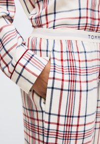 Pantalones de pijama a cuadros en blanco, rojo y azul, con tela suave, cintura elástica y bolsillos laterales. Sutil detalle de la marca en la cintura.