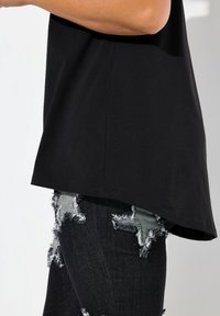 Sort, kortærmet top med buet kant, parret med slidte denimjeans med stjerneudskæringer og flossede kanter.