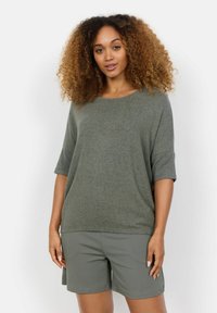 Haut vert olive à manches courtes en tissu doux, avec un col rond et une coupe décontractée. Associé à un short gris assorti.