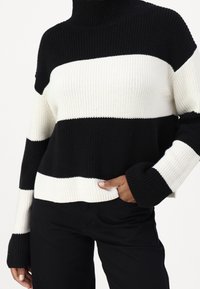 Maglione a collo alto a righe nere e crema, in maglia con texture a costine, caratterizzato da maniche ampie e una vestibilità rilassata.