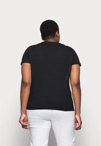 Sort kortærmet t-shirt lavet af bomuld. Klassisk rundhalsedesign med en glat struktur. Bæres med hvide bukser, vist fra ryggen.