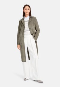 Suede trench coat in gray-green, featuring a notched collar, double-breasted buttons, and side pockets, paired with white wide-leg trousers.