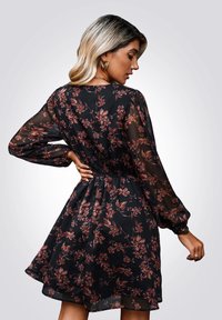 Vestido negro con flores que presenta mangas largas de tul, una cintura fruncida y una falda acampanada. El patrón incluye flores en tonos rosa y burdeos.