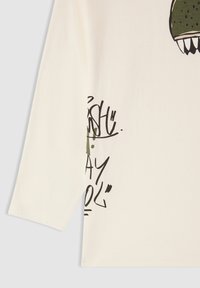 Kremowa koszula z długim rękawem z bawełny, z zielonym i czarnym wzorem graficznym oraz tekstem, a także teksturowanym akcentem wzdłuż dołu.