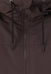 Brązowa kurtka z przednim zamkiem błyskawicznym, ściąganym kapturem i czarnymi troczkami. Materiał wygląda na gładki, z minimalnymi szwami.