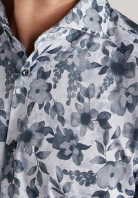 Koszula z kołnierzykiem uszyta z lekkiego materiału, ozdobiona monochromatycznym wzorem kwiatowym w odcieniach niebieskiego i szarości, z guzikami z przodu.