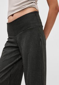 Czarno-białe spodnie w paski z wysokim stanem i miękką, gładką fakturą. Paski są cienkie i równomiernie rozmieszczone, dodając kontrastu.