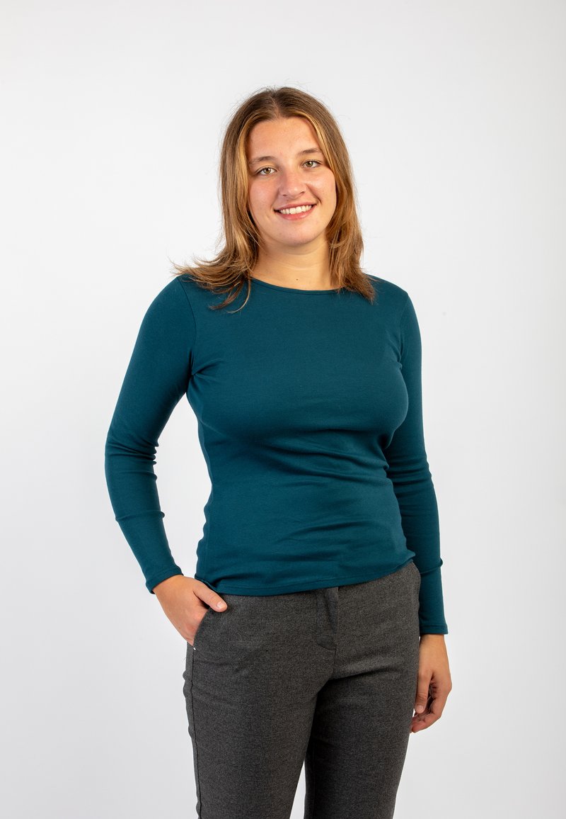 Camicia a maniche lunghe color turchese con scollo rotondo, taglio aderente, abbinata a pantaloni grigi scuri, tessuto liscio e senza motivi visibili.
